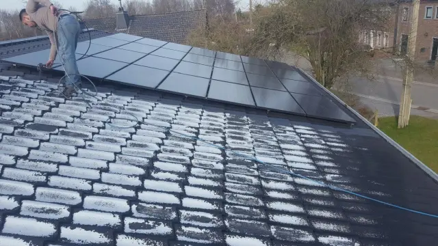 Facharbeiter reinigt ein dunkles Ziegeldach mit Reiniger/Schaum neben einer Photovoltaikanlage - Vorbereitung für die Standardbeschichtung.