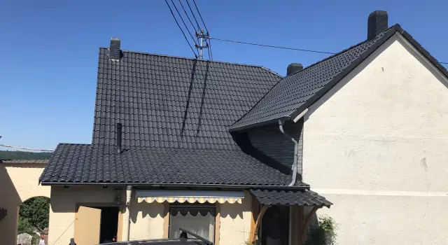 Einfamilienhaus mit frisch gereinigtem, dunkelgrau beschichtetem Ziegeldach bei klarem Himmel.