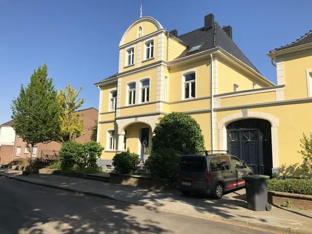 Sauber gereinigte, gelb-weiße Stadtvilla mit dunklem Dach und glatter, versiegelter Fassade bei Sonnenschein.