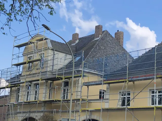 Historische Stadtvilla mit gelber Putzfassade und eingerüsteter Front während der Fassadenreinigung.